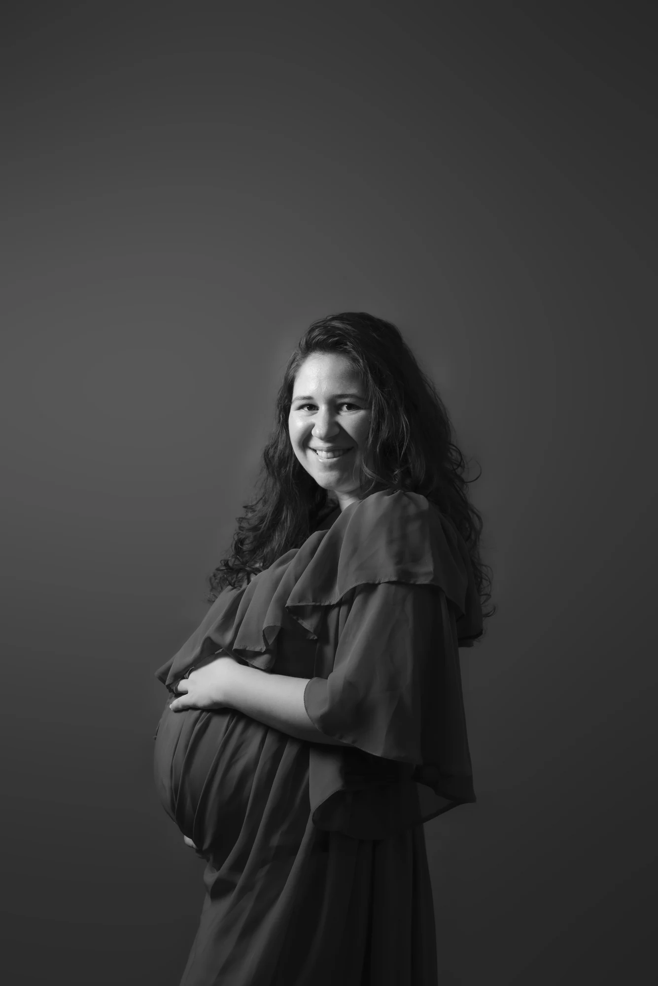 Portret alb-negru al unei femei însărcinate, fotografiată în studio.