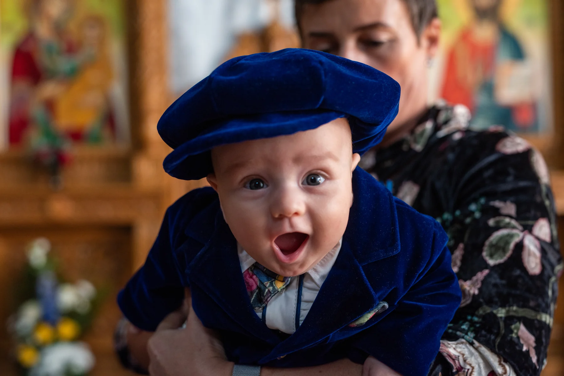 Bebeluș în ținută albastră, privind zâmbitor spre obiectiv la botez.